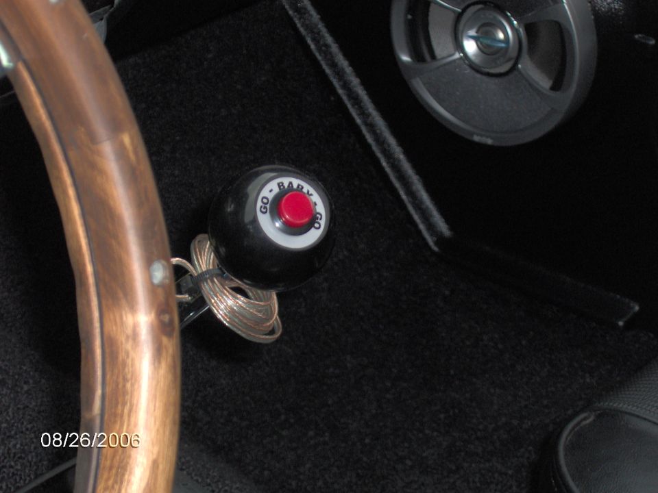 Black eight-ball style shifter knob reading GO BABY GO with red button, wood steering wheel above