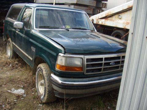 1993 Ford Bronco - Green Ford Bronco with a dented hood and chrome bumper sits in a yard with other vehicles in the background.