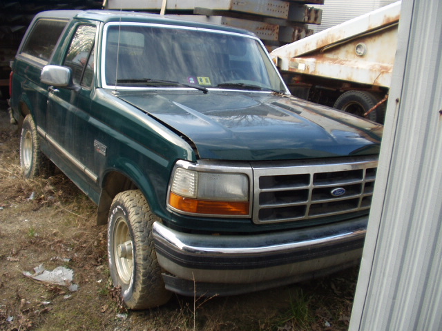 Green Ford Bronco with dented hood and chrome bumper