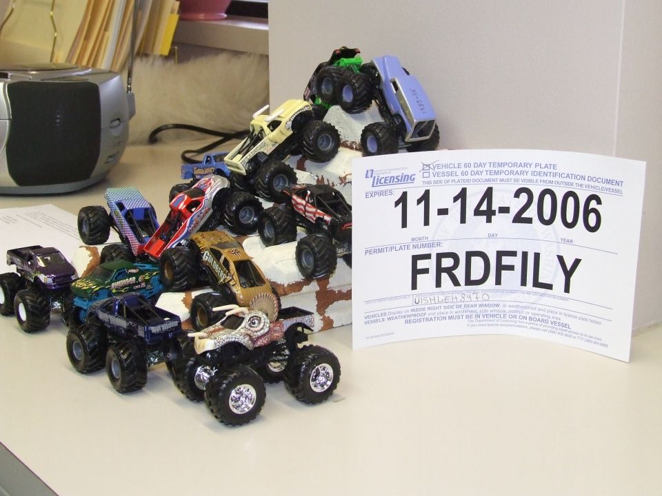 Collection of toy monster trucks piled on a surface next to a temporary vehicle registration document