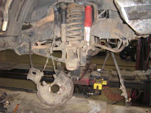 1995 Ford Bronco - Front suspension and brake parts are disassembled, showing the shock absorber and coil spring.