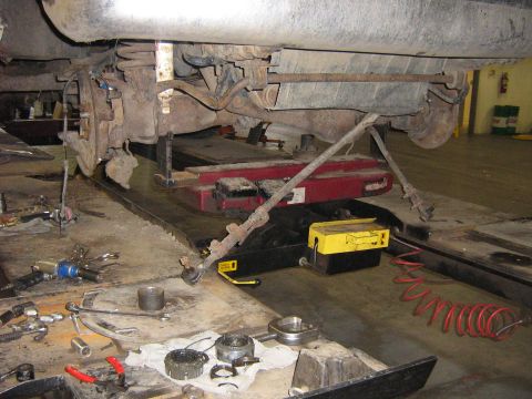 1995 Ford Bronco - The undercarriage of a 1995 Ford Bronco is shown with the ball joint removed and various tools laid out on the shop floor.