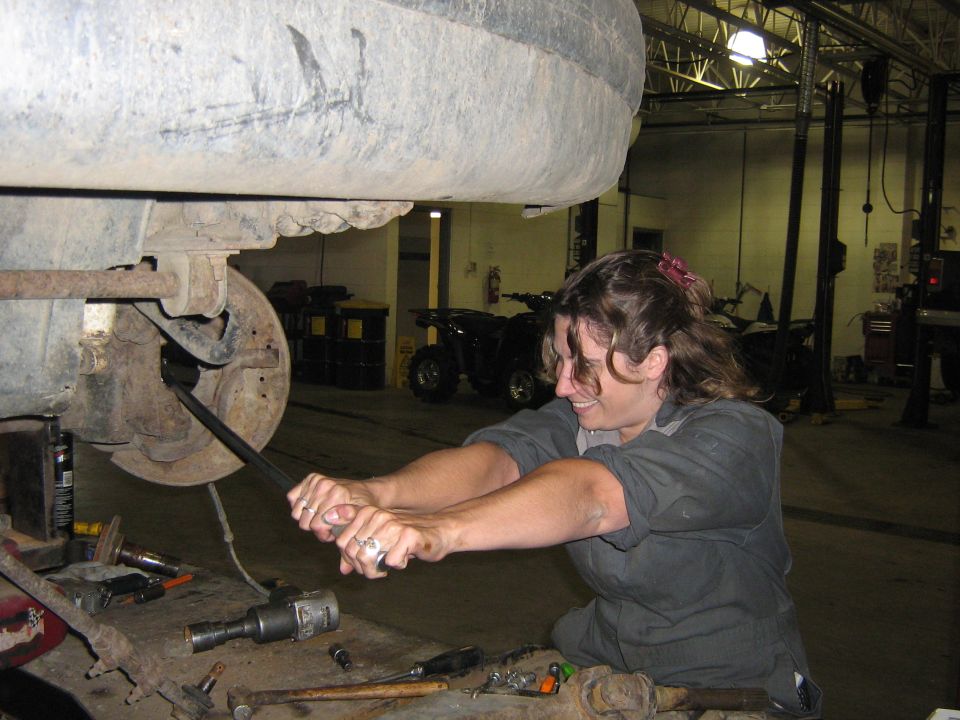 Woman using a breaker bar on a vehicle's suspension components in a garage