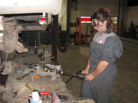 1995 Ford Bronco - A mechanic works on a vehicle suspension part at a workbench in a garage.