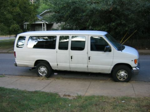 1994 Ford Bronco - A white van is parked on the side of the road with its front driver's side tire flat.