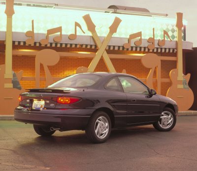 2002 Ford Escort - Dark coupe with a spoiler parked in front of a building decorated with musical notes and guitars.