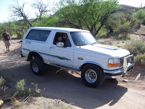1996 Ford Bronco - A white 1996 Ford Bronco with FX4 badging is seen driving on a dirt road in a dry, arid environment.