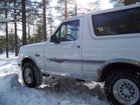 1996 Ford Bronco - A white 1996 Ford Bronco is seen in a snowy wooded area, with snow piled up around its tires.