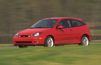 2002 Ford Focus - A red hatchback car is captured in motion on a grassy area, showing motion blur.