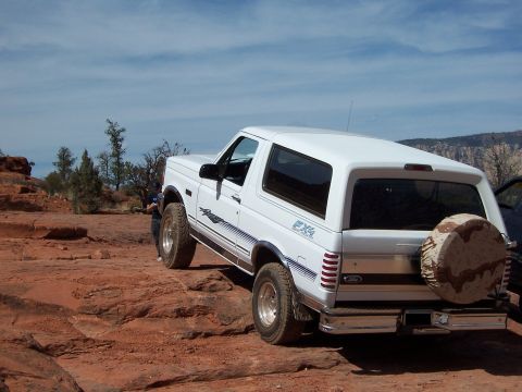 1996 Ford Bronco - A white 1996 Ford Bronco is parked on a rocky, desert terrain under a blue sky.