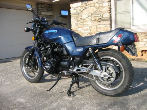 1985 Ford LTD Crown Victoria - A blue Suzuki GS1100E motorcycle is parked on a concrete surface in front of a stone-clad building.
