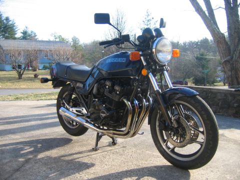 1985 Ford LTD Crown Victoria - A dark blue Suzuki motorcycle is parked on a concrete surface with a residential background.