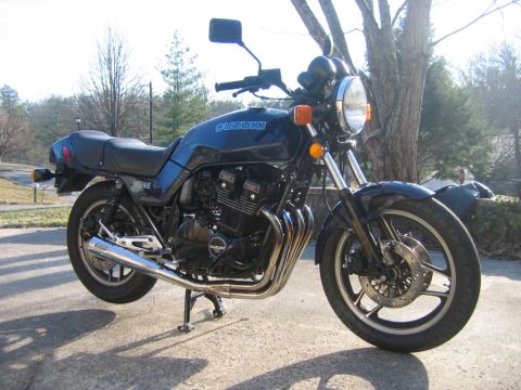 1985 Ford LTD Crown Victoria - A dark blue 1983 Suzuki GS1100E motorcycle is parked outdoors on a paved surface.