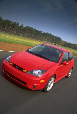 2002 Ford Focus - A red 2002 Ford Focus SVT is captured in a three-quarter front view on a race track, with trees and a grassy field in the background.