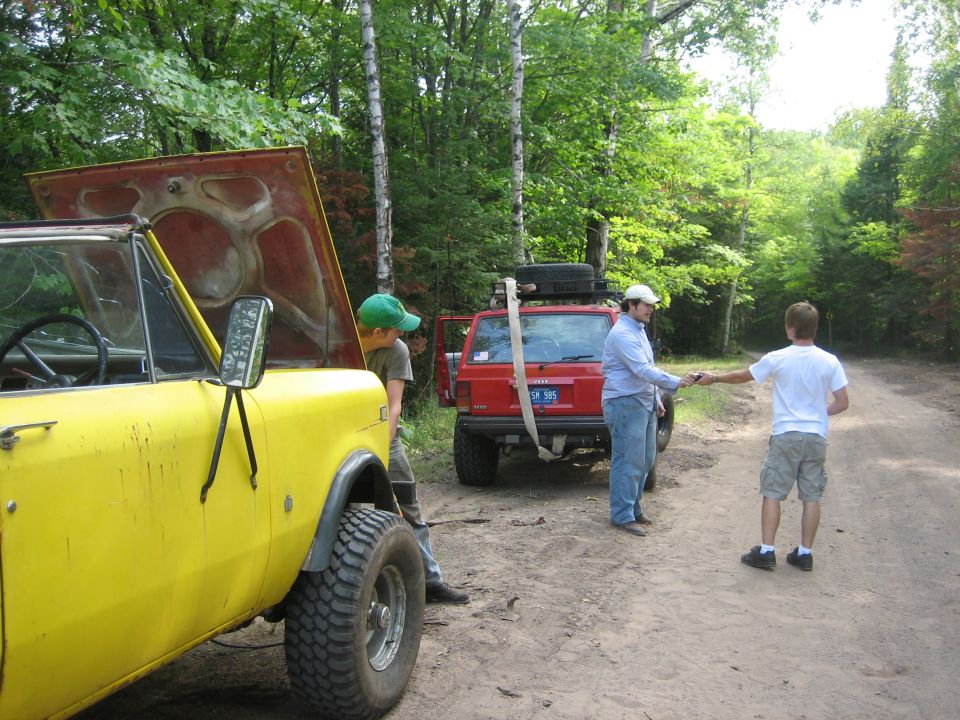Yellow off-road vehicle front quarter view with hood open, red SUV behind
