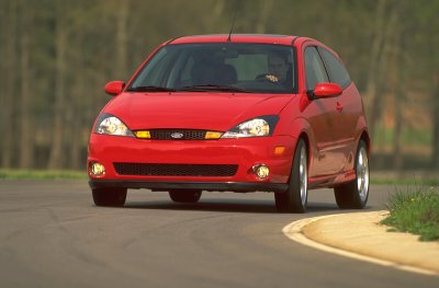 2002 Ford Focus - A red 2002 Ford Focus SVT hatchback is captured from the front as it drives on a paved road with trees in the background.
