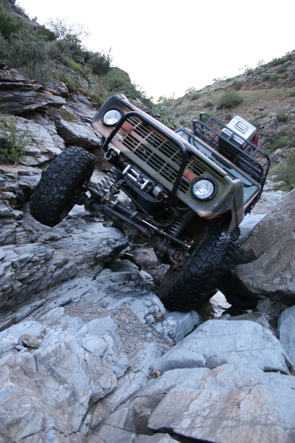 Camo early Ford Bronco crawling rocks from below, front axle and winch exposed