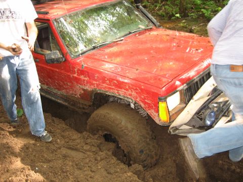 1997 Dodge 1500 - A red Jeep Cherokee is stuck in thick mud, with people attempting to help.