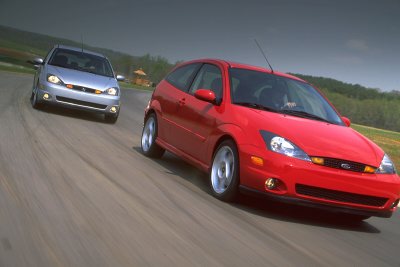 2002 Ford Focus - A red 2002 Ford Focus SVT is captured in a dynamic shot on a track, with a silver Focus following closely behind.