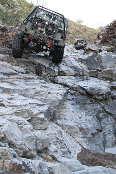 1966 Ford Bronco - Off-road vehicles tackle a challenging rocky trail in a desert landscape.