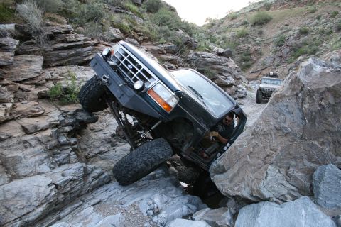 1966 Ford Bronco - An off-road vehicle navigates a challenging rocky path, with another vehicle visible in the distance.