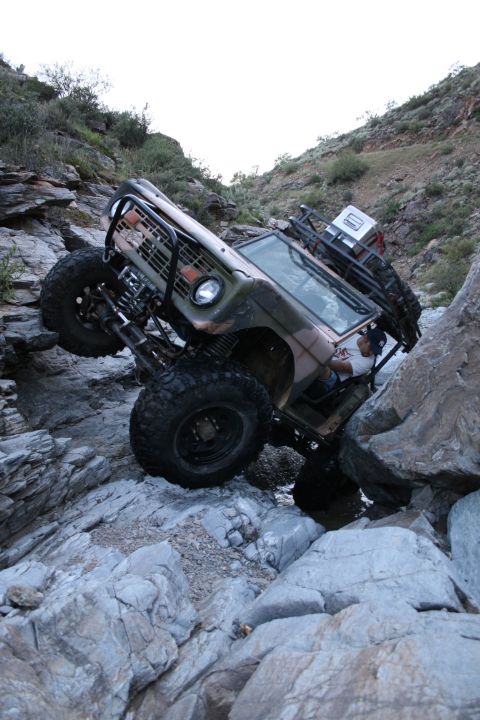 1966 Ford Bronco - A 1966 Ford Bronco navigates a rocky, off-road trail with its tires angled on large boulders.