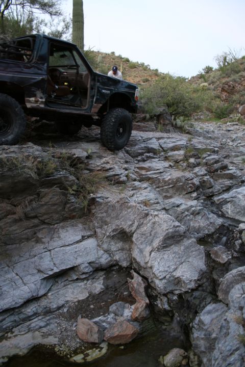 1966 Ford Bronco - A person stands by an off-road vehicle navigating a rocky, desert-like landscape.