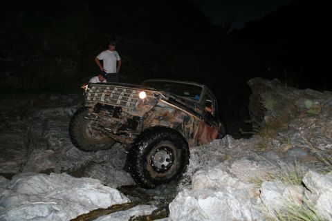 1966 Ford Bronco - A heavily modified off-road vehicle navigates a challenging rocky path in the dark.