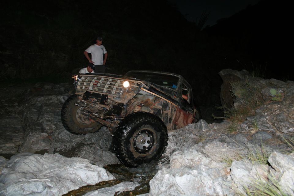 Fenderless red-primer Ford 4x4 crawling a rock ledge at night with spotters watching