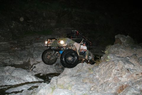 1966 Ford Bronco - An off-road vehicle with a roll cage and large tires is driven over a rocky obstacle course at night.