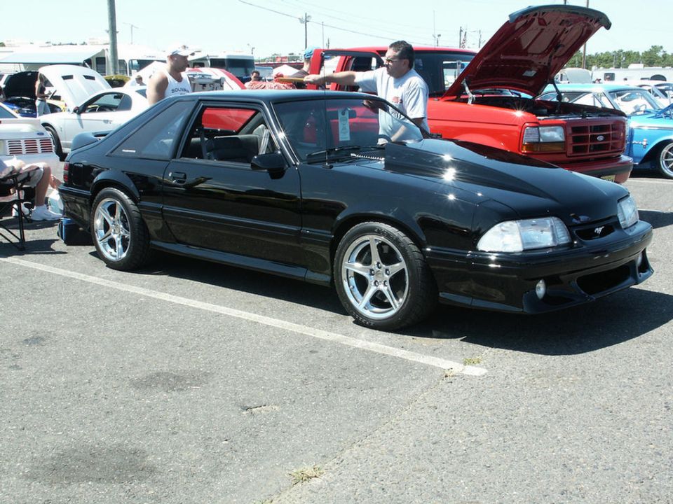 Black coupe with a hood scoop and aftermarket wheels parked at a car show