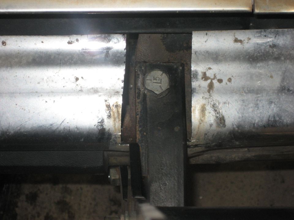 Close-up of a rusty metal bracket bolted to a vehicle's frame, showing signs of wear and tear