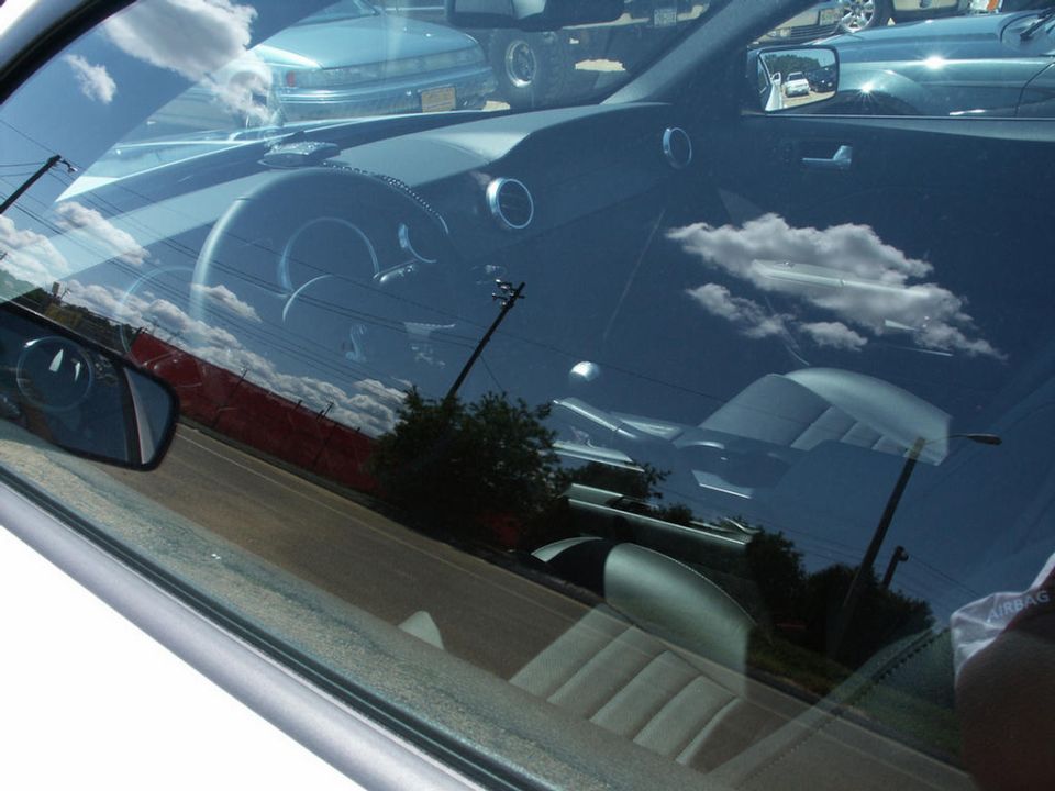 Interior view of a car, showing the steering wheel, dashboard, and seats. Clouds are reflected in the windshield