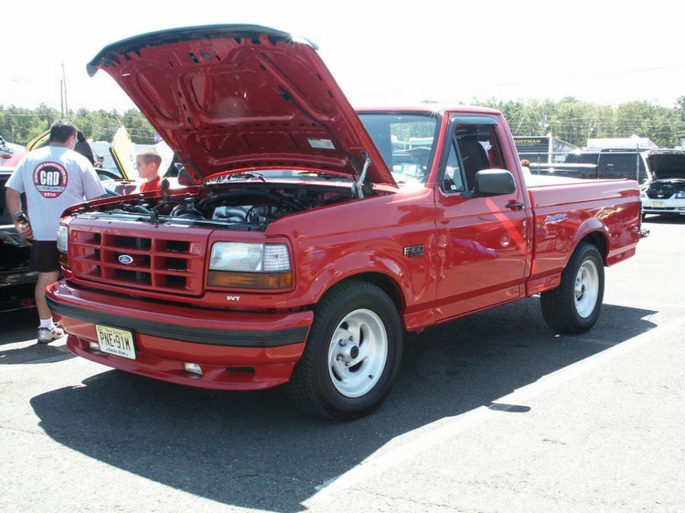 Red pickup truck with hood open, white wheels, and a "SVT" badge