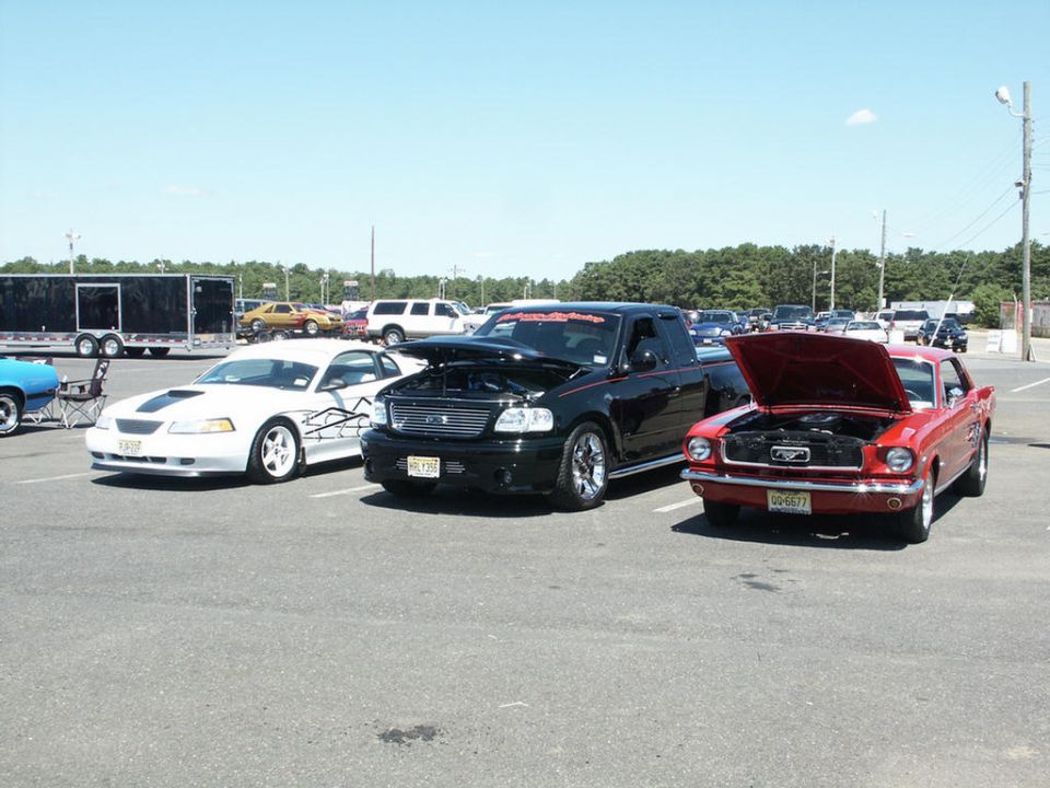 Red 1960s Mustang, black pickup truck, and white Mustang parked outside