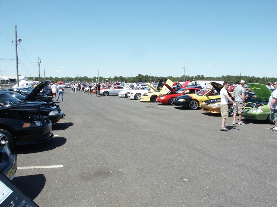 Cars parked in rows at an outdoor car show under a clear blue sky