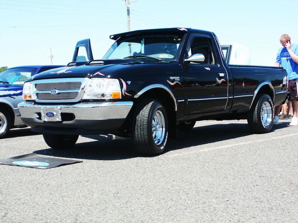 Black Ford Ranger pickup truck with chrome accents and aftermarket wheels. Another vehicle is partially visible to the left