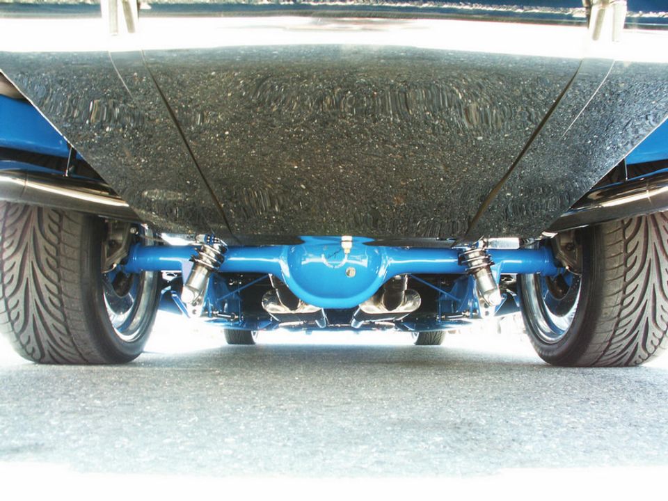 Blue rear axle with dual shocks and exhaust pipes under a car with black speckled undercarriage