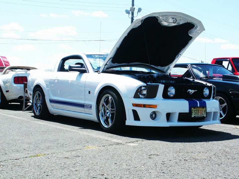 White Ford Mustang with blue racing stripes and hood open, parked next to other cars