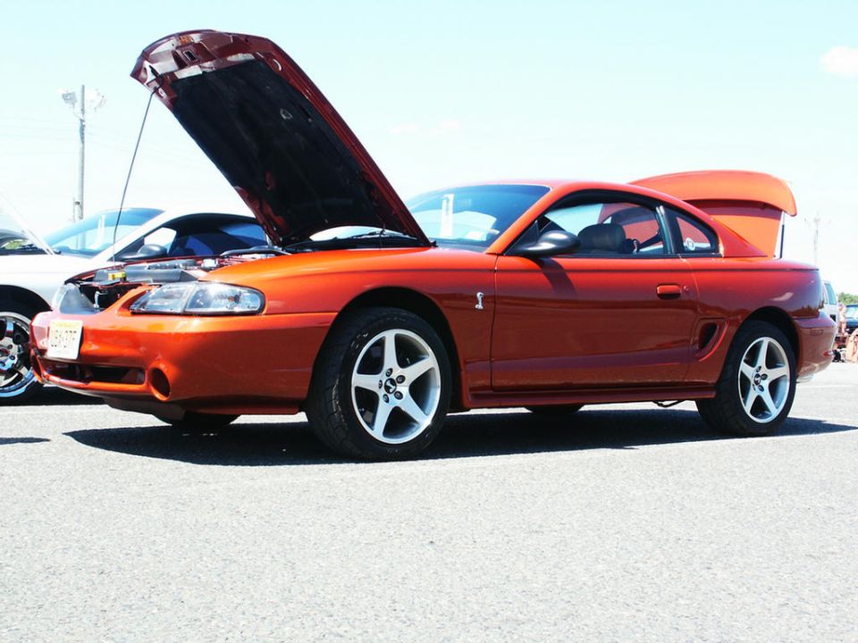 Orange coupe with hood and trunk open, side view, five-spoke wheels, visible "S" emblem