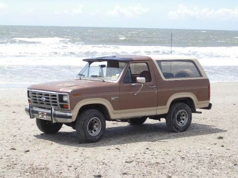 1985 Ford Bronco - This 1985 Ford Bronco is parked on the beach, with the ocean waves visible behind it.