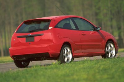 2002 Ford Focus - A red 2002 Ford Focus hatchback is shown from the rear quarter angle, parked on a grassy shoulder.