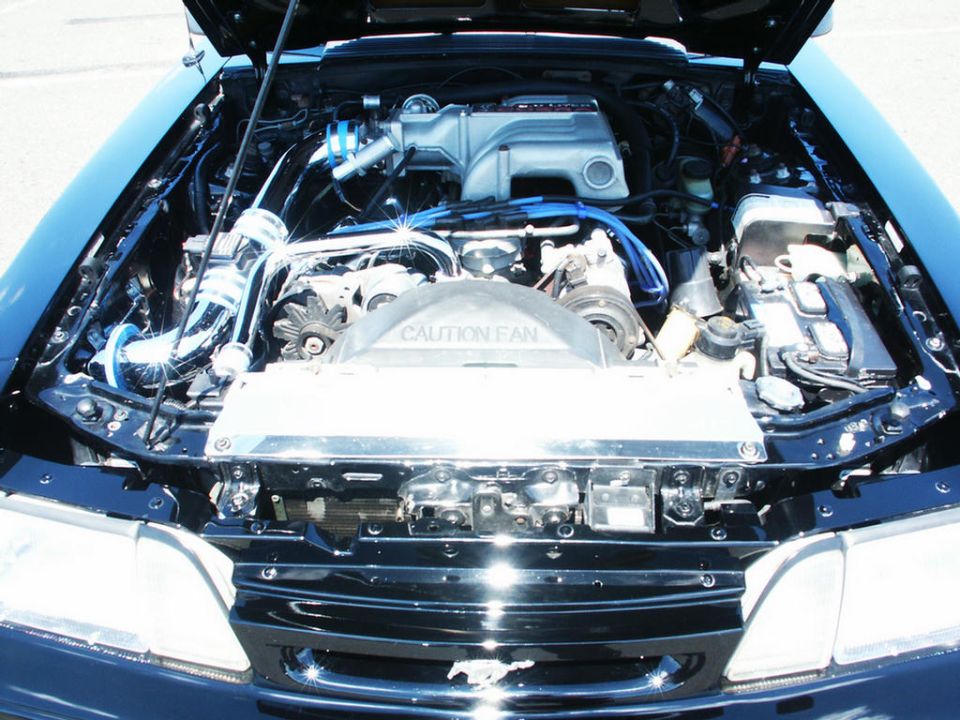 Engine bay with V8 engine, chrome intake, and blue spark plug wires. Fan shroud has 'CAUTION FAN' text