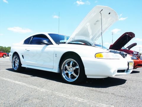2001 Mercury Grand Marquis - A white Ford Mustang is parked with its hood open at an outdoor car show.