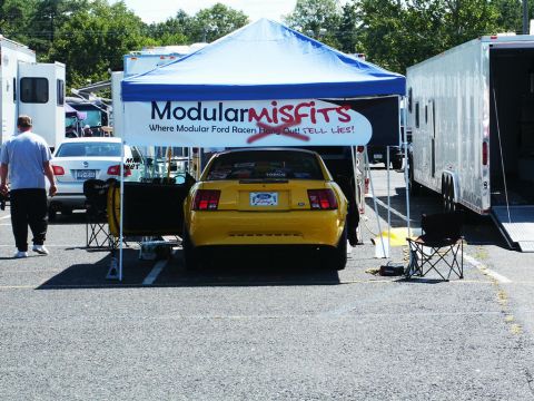 2001 Mercury Grand Marquis - A yellow Ford Mustang is parked under a tent at a car show.