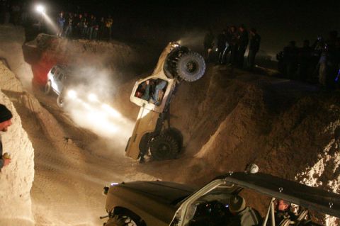 1987 Suzuki Samurai - Spectators watch as off-road vehicles navigate a challenging dirt course in the dark.