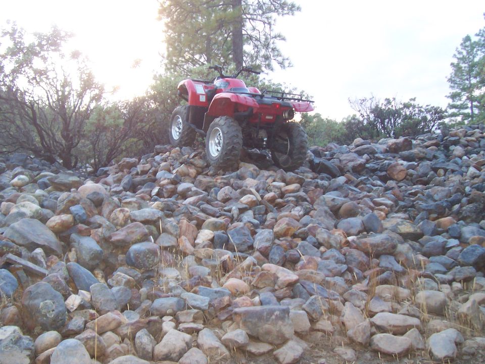 Red ATV parked on a pile of rocks with trees in the background
