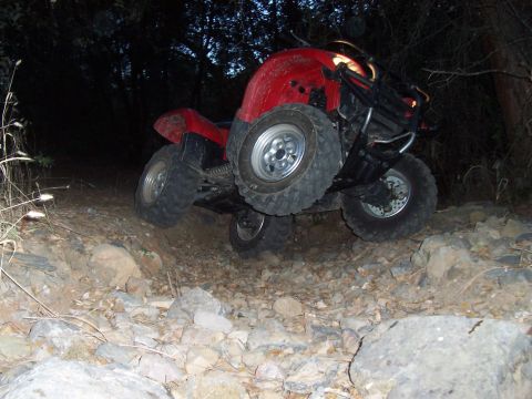 1994 Ford F-150 - A red quad bike is shown traversing a difficult, rocky path in a wooded area at dusk.