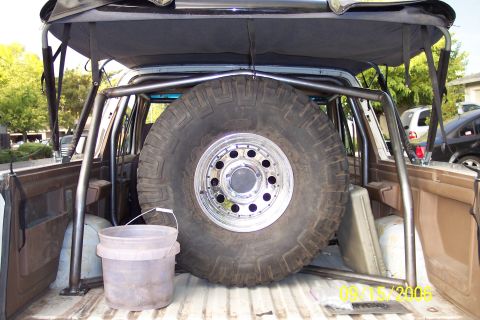 1989 Ford Bronco - The rear interior of a vehicle is shown, a large spare tire mounted vertically and a custom roll cage structure.