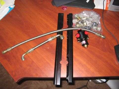 1991 Ford Bronco - A collection of automotive parts, including a fuel filter and braided lines, are laid out on a wooden surface.
